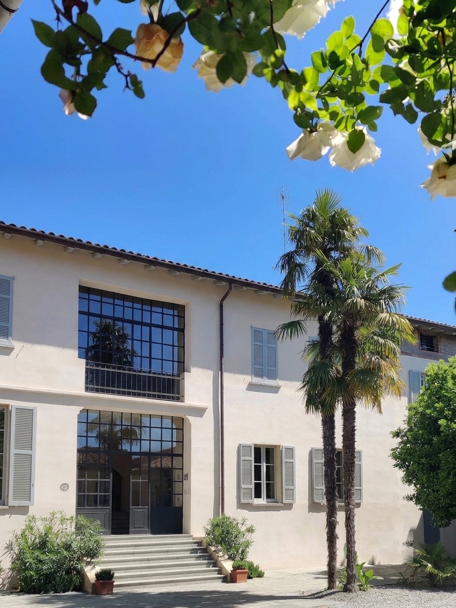 The villa facade and palms under a clear sky, seen from the gravel courtyard