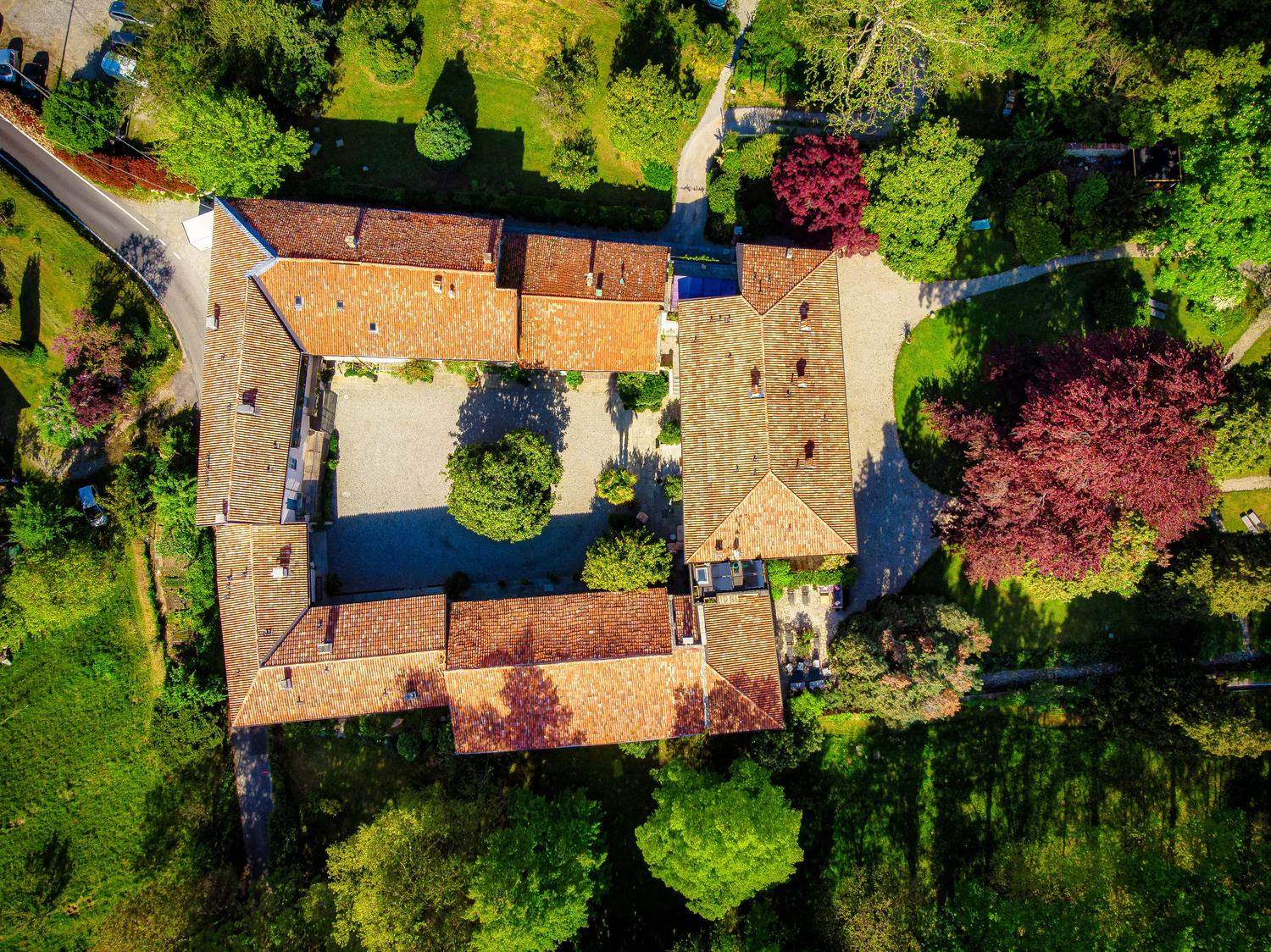 The 15th-century farmhouse seen from directly above: four ranges of tiled roofs closed around the gravel courtyard with its tree, the park and old copper beeches all around