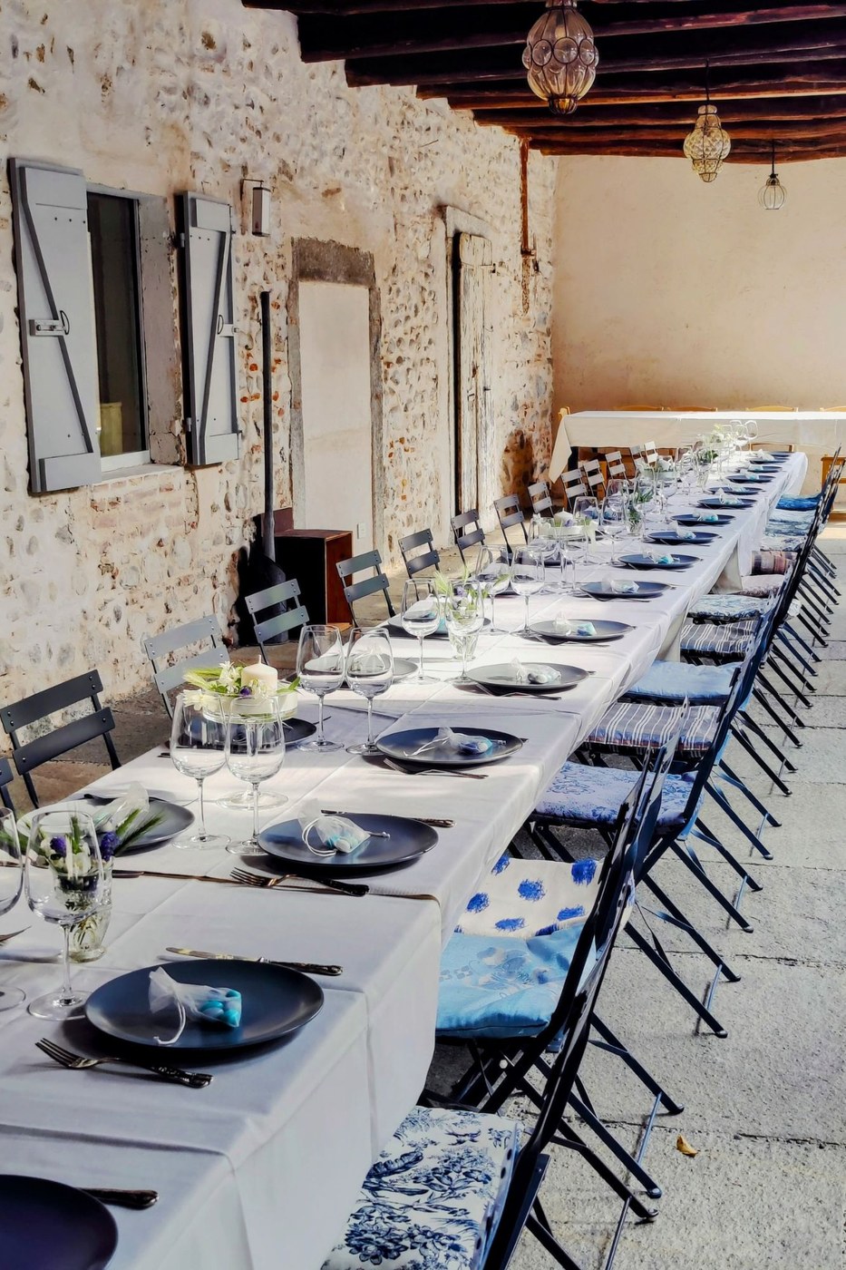 A long white-linen table running the length of the stone portico, laid with slate plates, wine glasses and blue and turquoise details