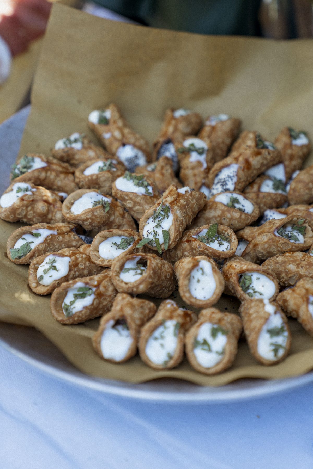 A platter of savoury cannoncini filled with soft cheese and scattered with herbs and poppy seeds, served on baking paper