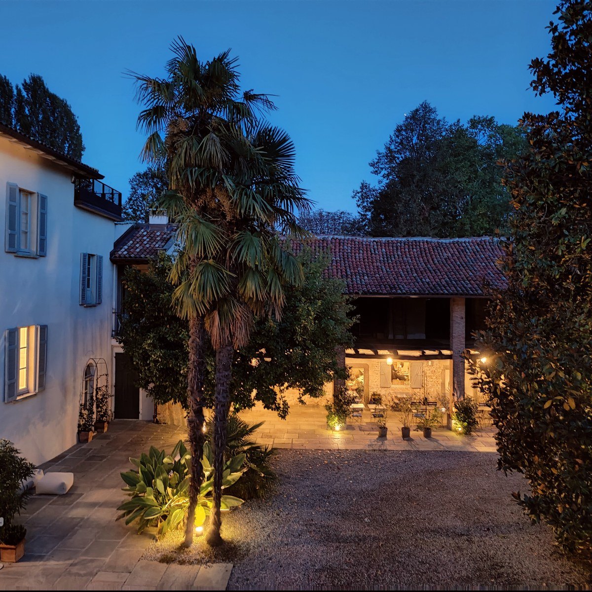 The courtyard and portico lit at blue hour, with the palm and the old hayloft